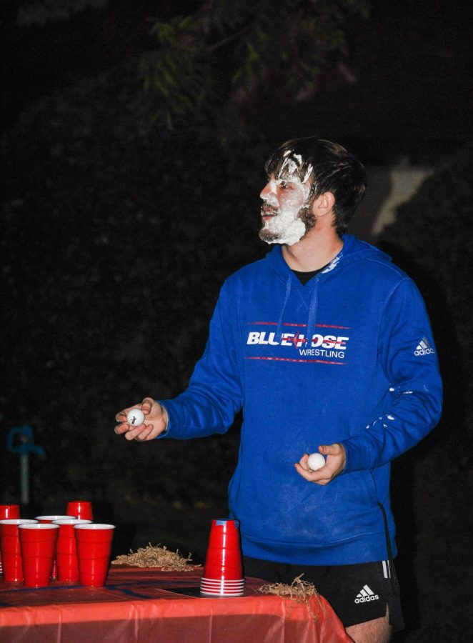 A PC student playing cup pong after being pied in the face.